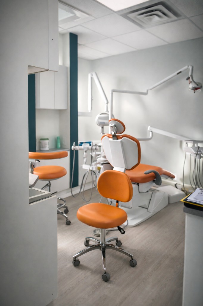 A treatment room at A+ Dental with an orange dental chair and stools